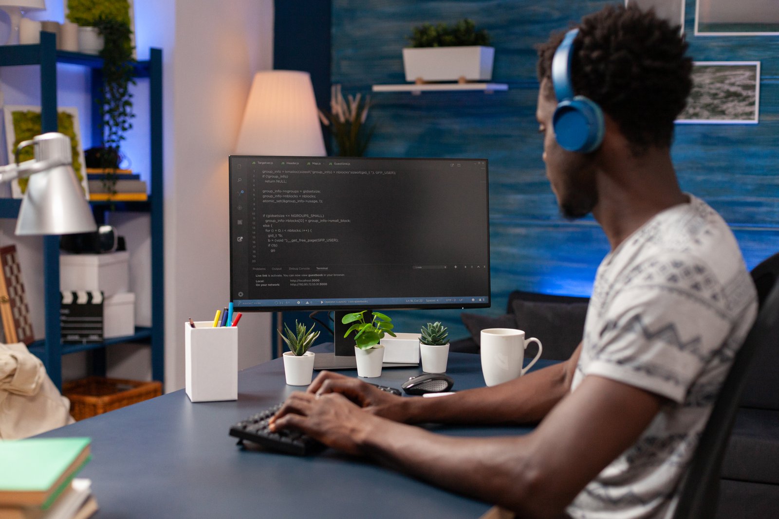 A young African American man programming on a desktop computer in a modern office lit with blue lights