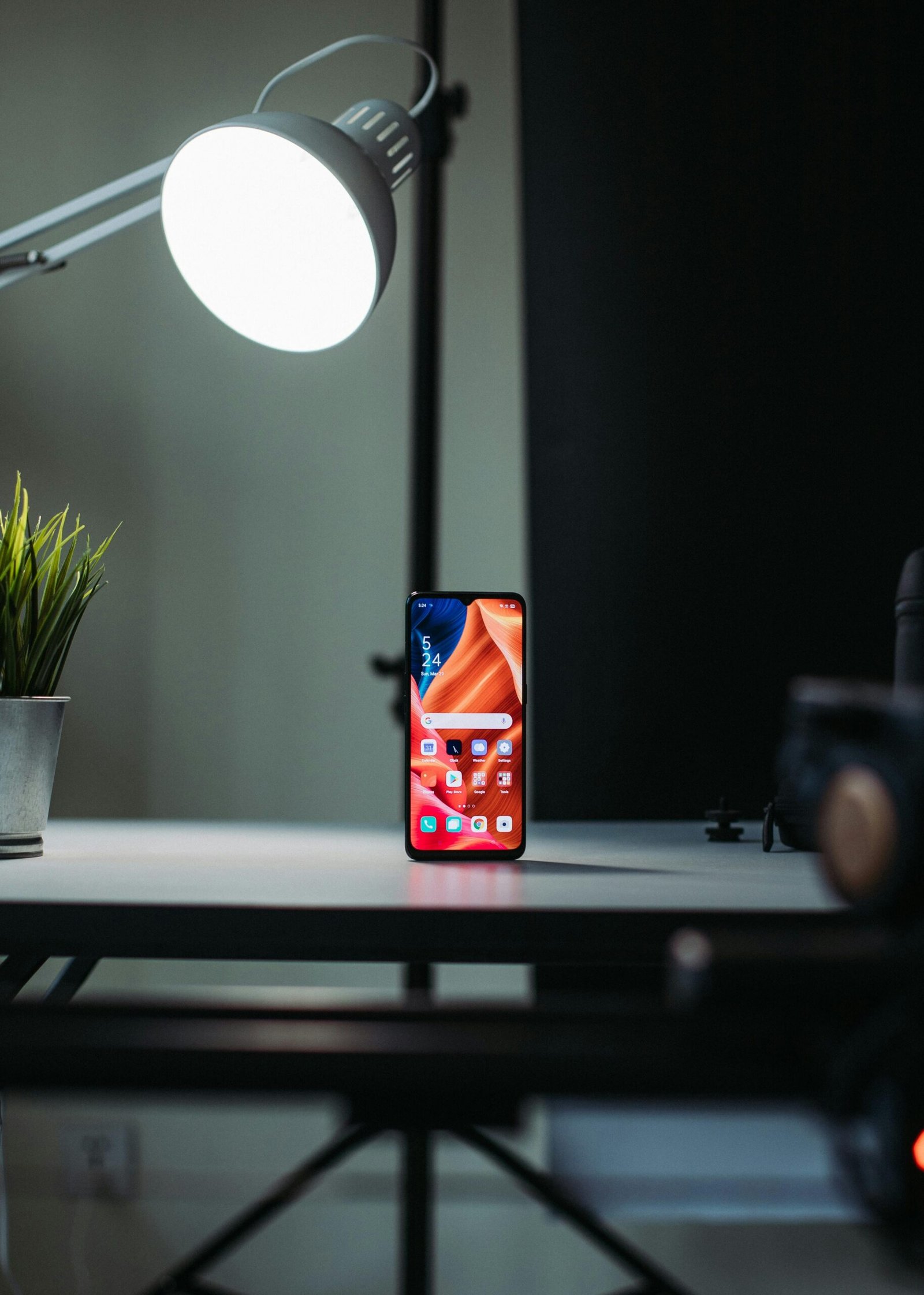 Modern smartphone displayed on a desk under a desk lamp, highlighting its vibrant screen and apps.